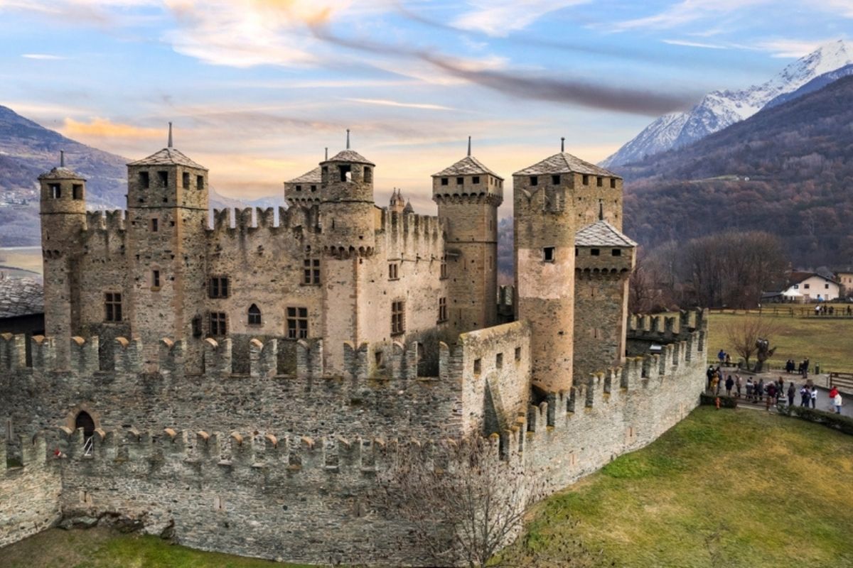 Vista panoramica del Castello di Fénis circondato da montagne, catturando l'essenza medievale del luogo.